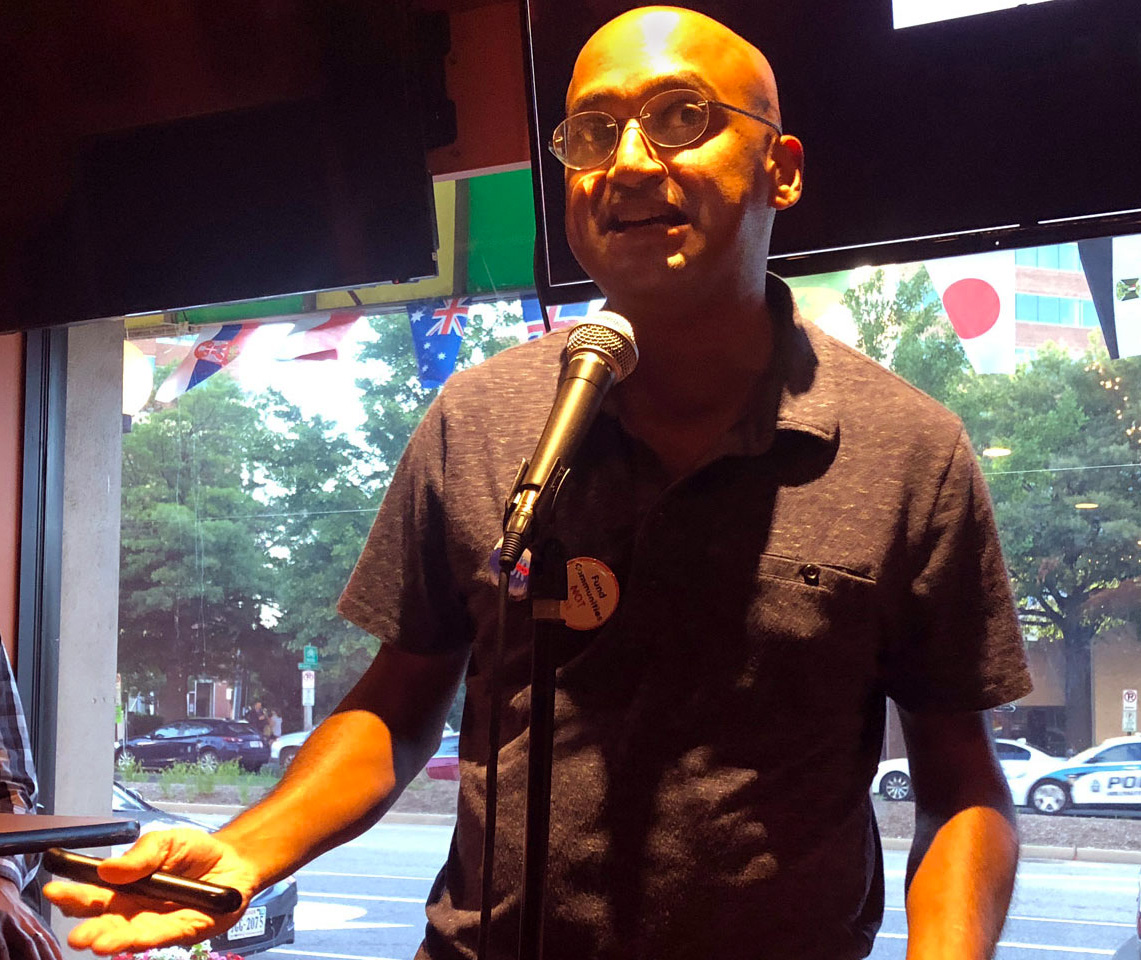 A picture of Roshan Abraham at a microphone speaking.