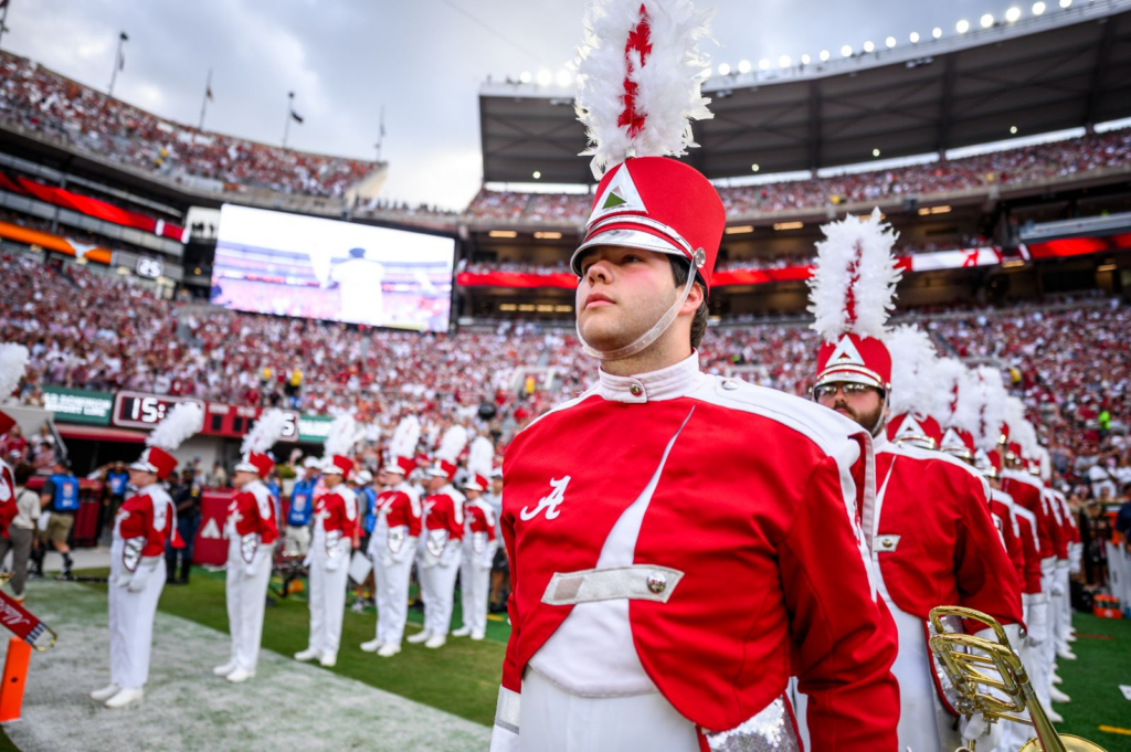 young man in crimson white Alabama band uniform, standing in formation in football stadium