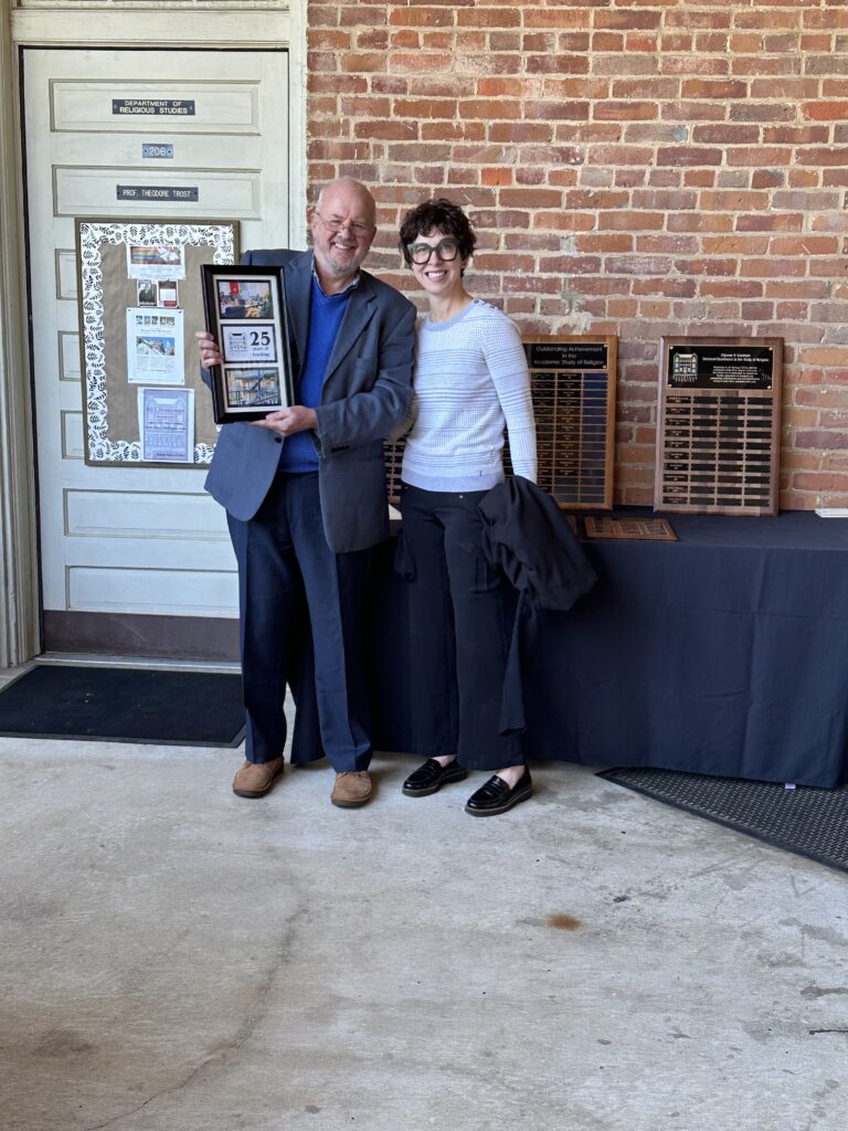 Photo of a professor receiving a framed set of photographs recognizing 25 years of teaching from another professor