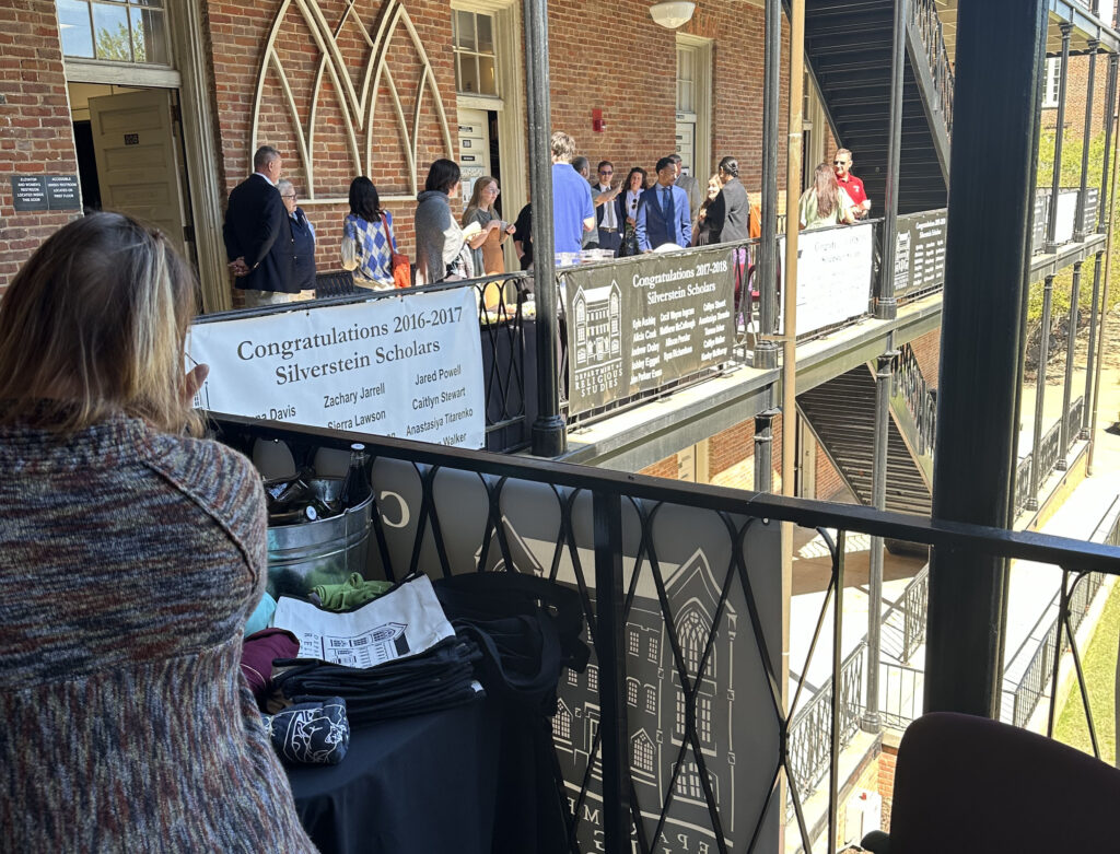 people talking and eating on the second floor balcony of a brick building with black iron railings