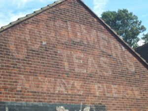 Red brick gable with faded white paint which states "Consumer's Teas Always Please"