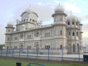 Photo of white stone exterior of gurdwara, showing motifs of Mughal arches and multiple domes and towers of the Sikh temple on Ford End Road, Queens Park, Bedford, Bedfordshire