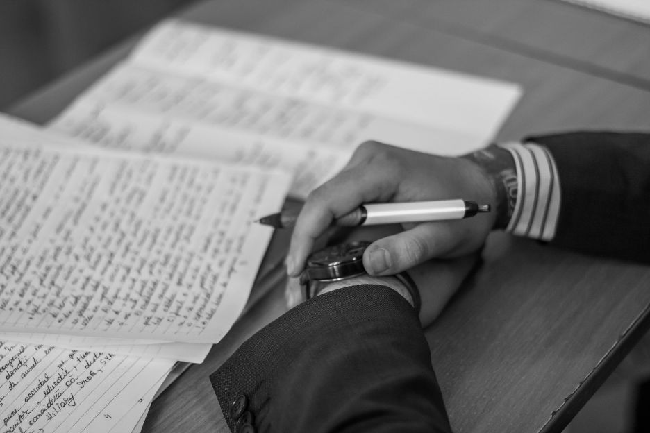 Black and white photo of hands holding pen and writing papers.